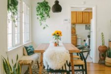 a cozy boho dining nook with simple wooden furniture, a tassel rug, greenery and a wicker lamp hanging over the table
