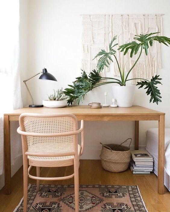 a cozy boho home office nook with a sleek desk, a rattan chair, a boho rug, a basket and a macrame hanging plus potted plants