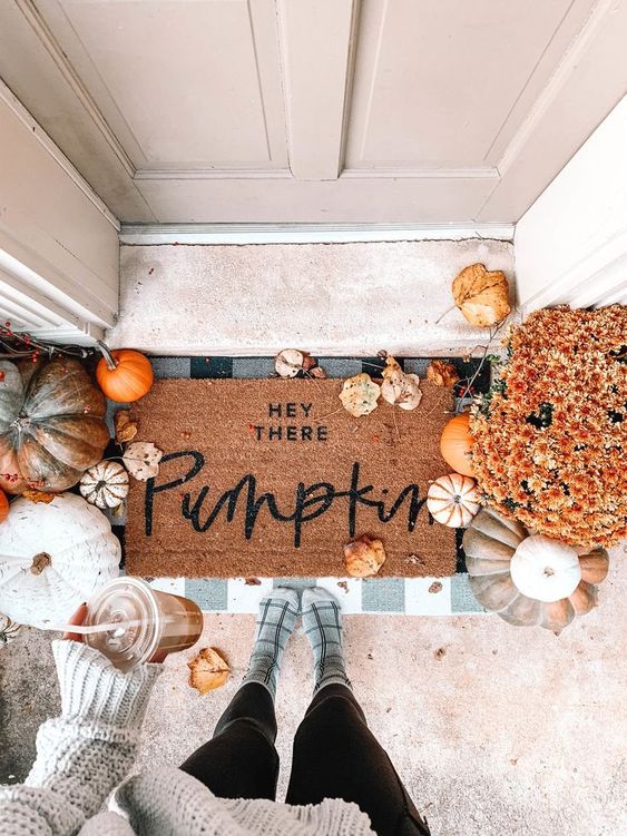 a cozy fall porch with lots of pumpkins, gourds and leaves, bright fall blooms and layered mats