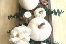 a dark stained woodne tray, white pumpkins, blooms, candles and acorns for a pretty fall centerpiece