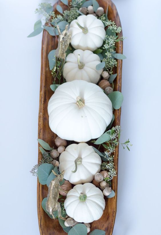 a dough bowl with pumpkins, eucalyptus and acorns is a cool fall centerpiece with a strong rustic feel