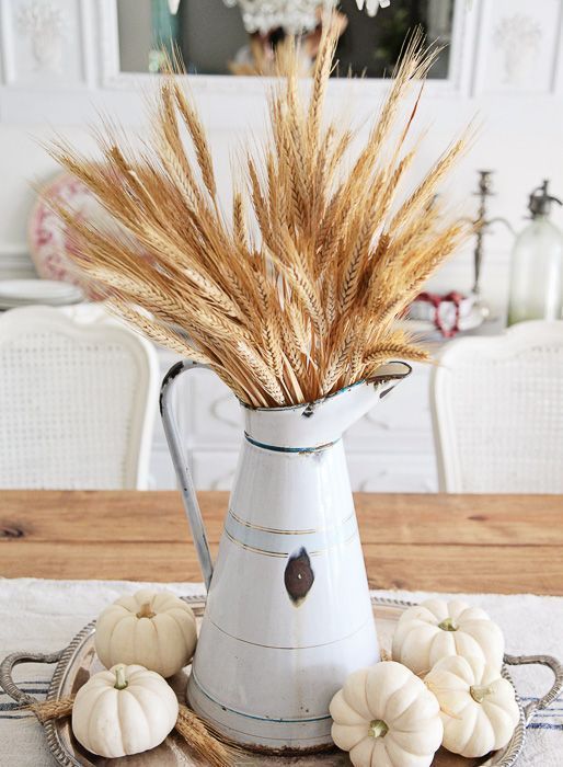 a fall centerpiece of a silver tray, white pumpkins, wheat and a wheat bundle in a metal jug is a chic idea