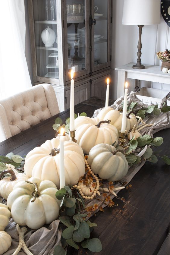 a fall centerpiece of a table runner, pumpkins, gourds, antlers, candles and beads is veyr lush and chic