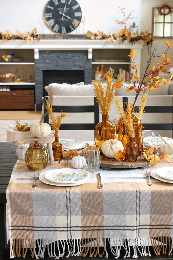 a fall tablescape with pumpkins, leaves, wheat on stands and trays looks very inviting and very cozy