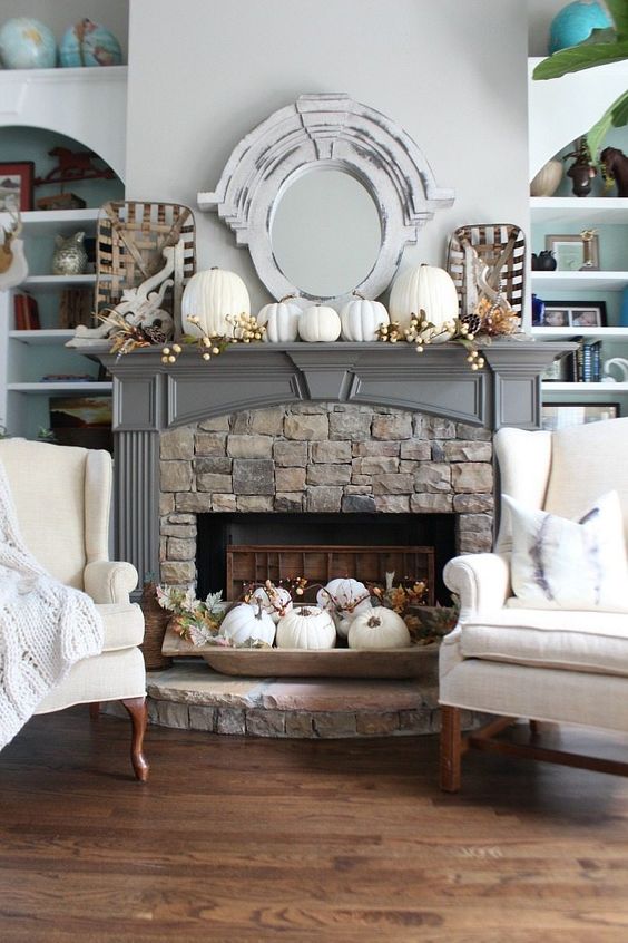 a fireplace styled with white pumpkins, berries, greenery and feathers and an additional arrangement in a dough bowl