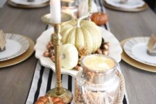 a glam fall centerpiece of a striped runner, fake pumpkins, nuts and acorns, candles and a mercury glass lantern