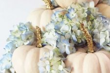 a glam fall centerpiece of a white stand with white pumpkins and gold glitter and blue hydrangeas is chic