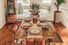 a gorgeous boho dining space with potted greenery, a boho rug, a wicker pendant lamp and warm-stained furniture