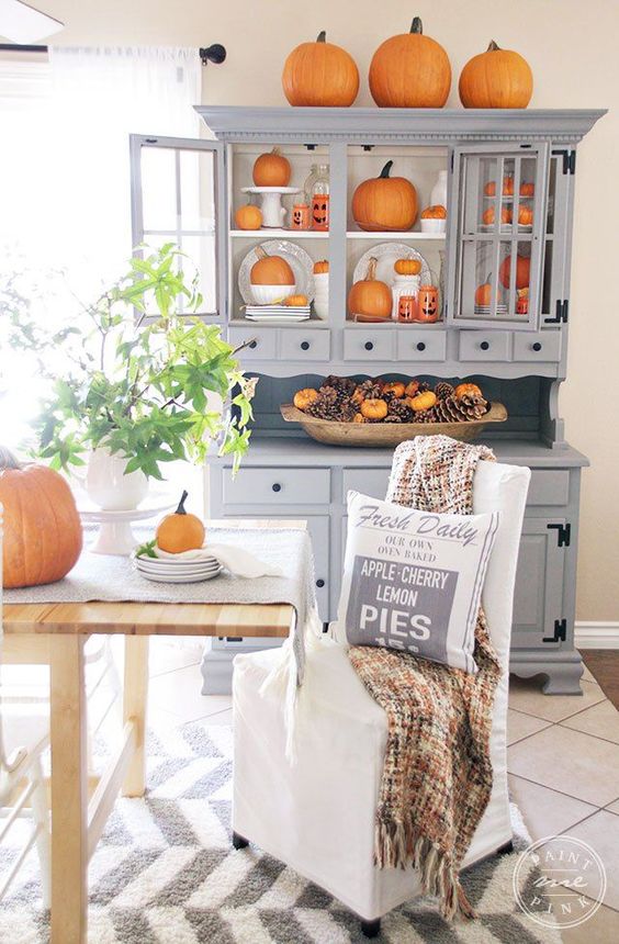 un buffet gris avec beaucoup de citrouilles orange, un bol de pâte avec des pommes de pin et de fausses citrouilles orange un buffet gris avec beaucoup de citrouilles orange, un bol de pâte avec des pommes de pin et de fausses citrouilles orange