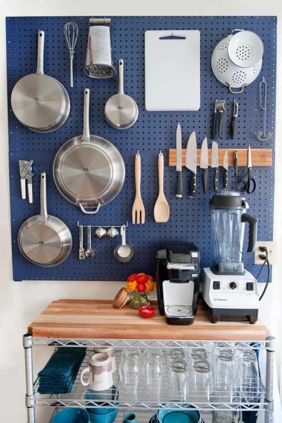 a large blue pegboard with hooks and hangers holding various pans, pots and other stuff is a great solution for a kitchen