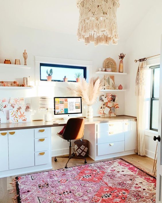 a light-filled boho home office with a desk with plenty of storage, open shelves, a boho rug, a macrame chandelier and pampas grass