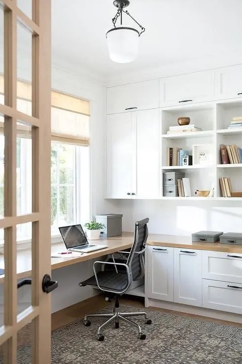 a lovely modern country home office with white kitchen cabinets used for storage, a floating desk and some simple shades plus a vintage lamp