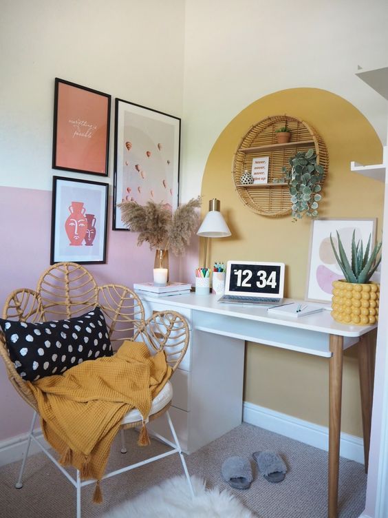 a mid-century modern boho home office with a gallery wall, a round rattan shelf, a desk, a rattan peacock chair and pampas grass