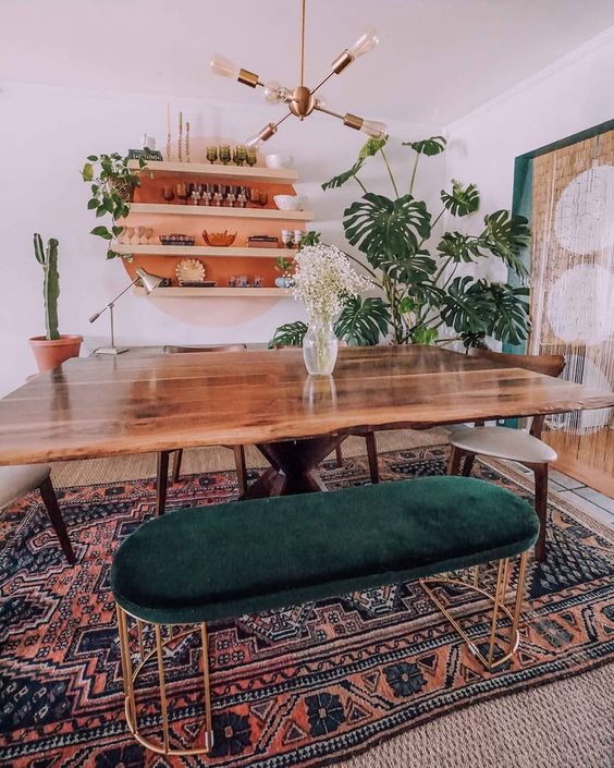 a mid-century modern meets boho dining room with a live edge table, a boho rug, a forest green ottoman and potted plants