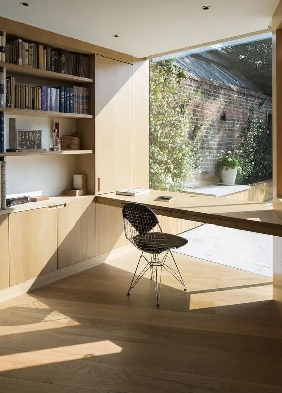 a minimalist home office with a built-in plywood storage unit with open storage compartments, a windowsill desk and a black chair