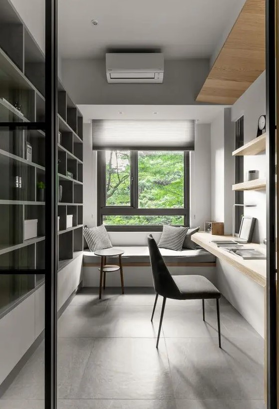 a minimalist home office with a windowsill daybed, a large storage unit, floating shelves and a desk, a grey chair