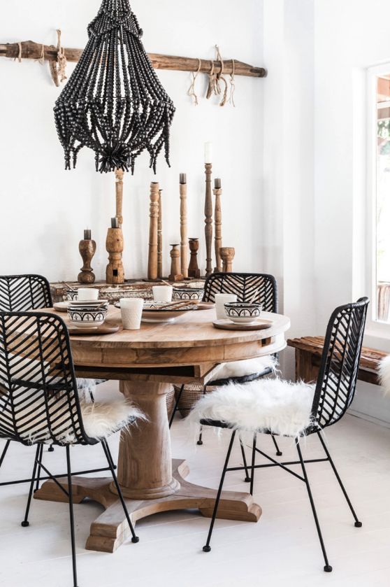 a modern meets boho dining space with a bead chandelier, rattan and wooden furniture, wooden candleholders