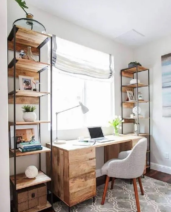 a modern rustic home office with a wooden desk and open shelving units, a printed rug, a grey chair and Roman shades