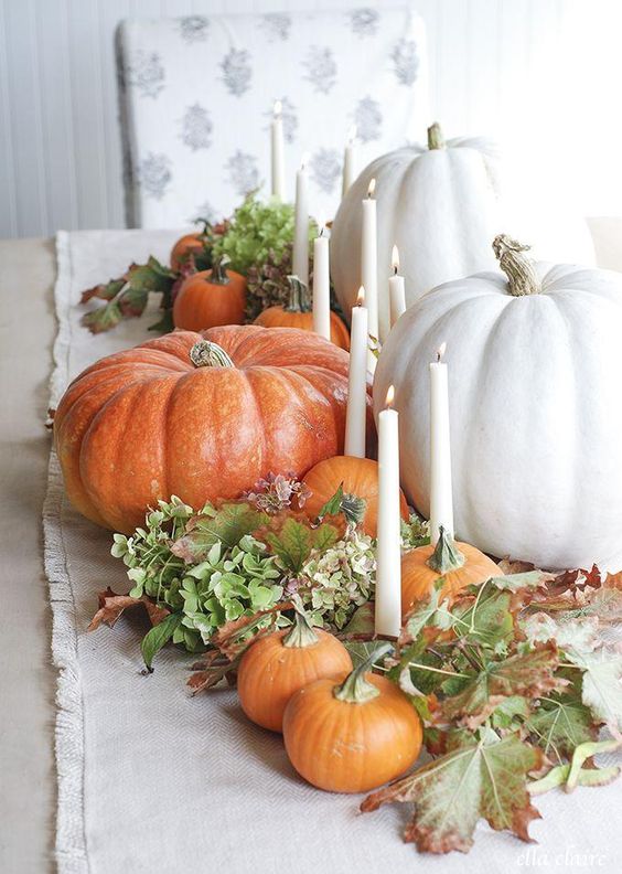 a natural fall centerpiece of various pumpkins, tall candles, green hydrangeas and fall leaves