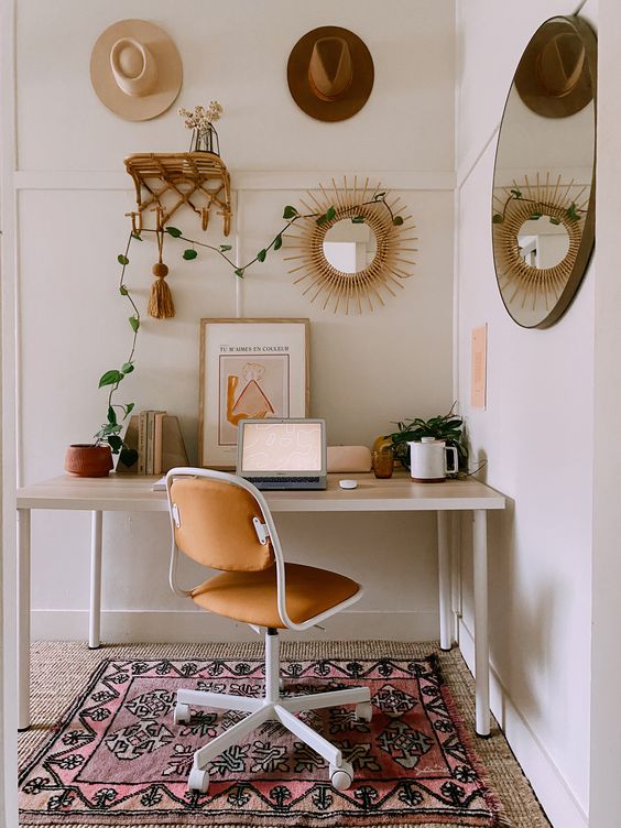 a neutral boho chic home office with a boho rug, a desk, a leather chair, hats, a rattan shelf and a sunburst mirror