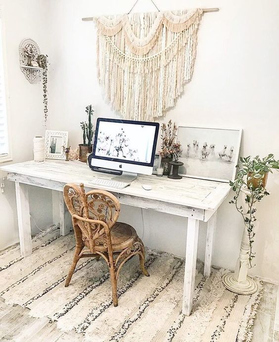 a neutral boho home office with a whitewashed desk, a unique rattan chair, a macrame hanging, potted plants and artworks