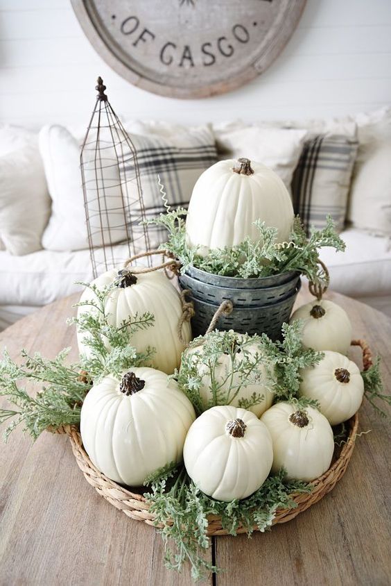 a neutral fall centerpiece of a basket with greenery, white pumpkins and a bucket with a pumpkin
