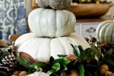 a neutral fall centerpiece of magnolia leaves, nuts, pinecones and a stack of pumpkins is cool