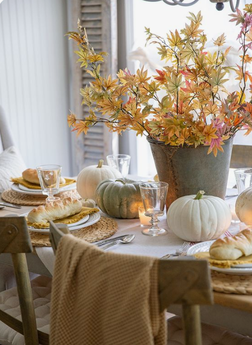 a neutral fall table with woven placemats, a fall leaf centerpiece, natural pumpkins and candles for coziness