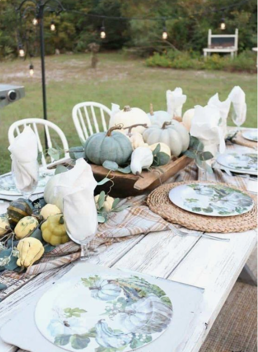 a neutral farmhouse table with woven palcemats, printed plates, natural veggies and pumpkins plus greenery