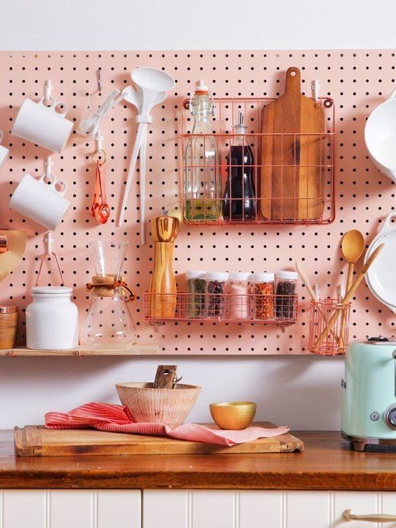 a pink pegboard hanging over the cabinets allows attaching a lot of shelves, hooks and wire holders
