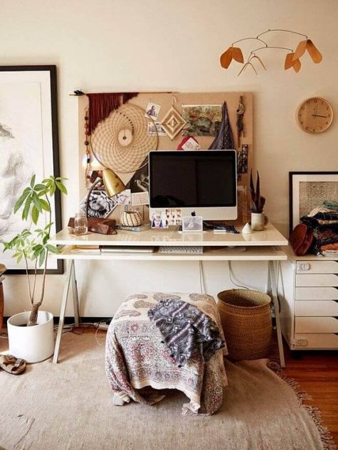 a relaxed boho office with a memo board with artworks, a boho stool and blanket, baskets and potted plants