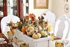 a rustic fall centerpiece of a white box with faux pumpkins, antlers, bold leaves and vine is vintage and elegant