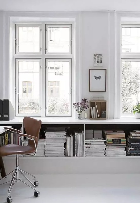 a simple Nordic white home office with a large open storage unit, a white desk and a brown leather chair