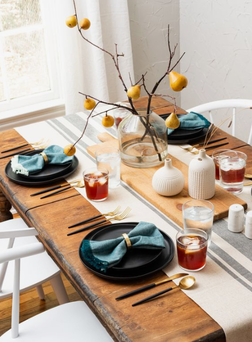 a simple fall tablescape with dark plates, blue napkins, a branch and pear centerpiece and white vases with wheat