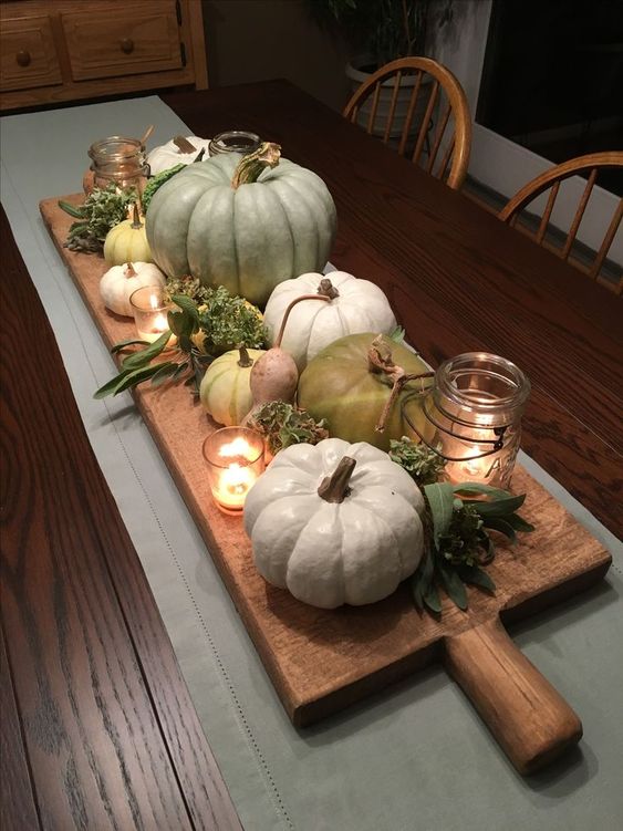 a simple farmhouse centerpiece of a wooden board with pumpkins, gourds, greenery, candles is lovely