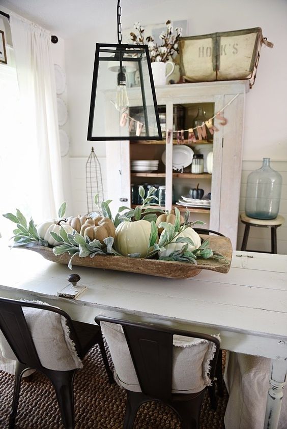 a simple rustic fall centerpiece of a dough bowl, greenery and neutral pumpkins will bring a fall feel to the space