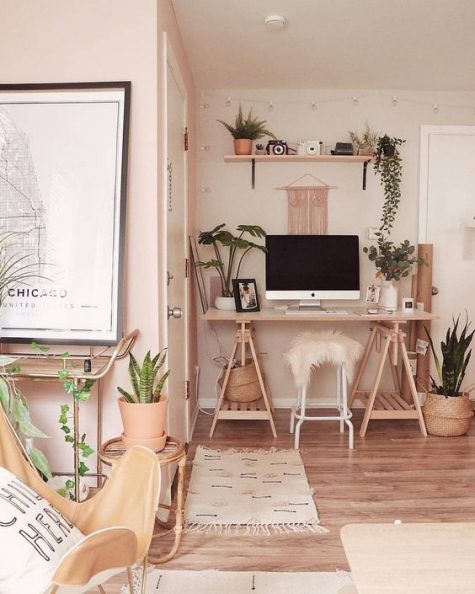 a warm-colored boho space with a wooden trestle desk, an open shelf, potted greenery and plants and long fringe