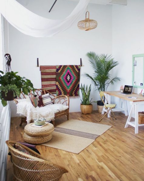 a welcoming boho space with a trestle desk, colroful rugs, potted plants, rattan and jute furniture