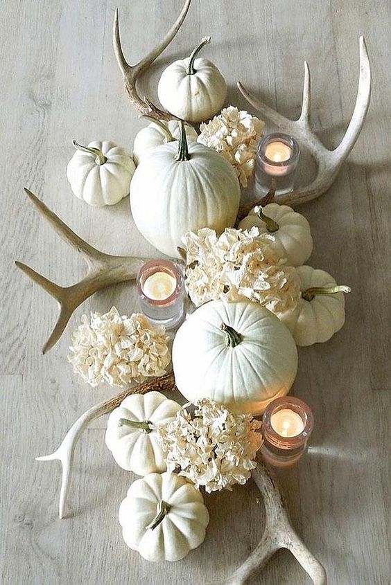 a white fall centerpiece of white hydrangeas, antlers, pumpkins and candles is chic and wow