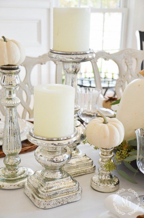a white fall centerpiece of white pillar candles and white pumpkins in mercury glass stands