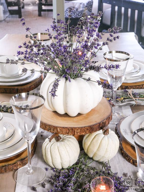 a white pumpkin vase with lavender on a wood slice, more white pumpkins under it for a fall table