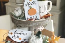 a whitewashed wooden stand with faux pumpkins, fall leaves, greenery in a mug, tags, knit pumpkin caps