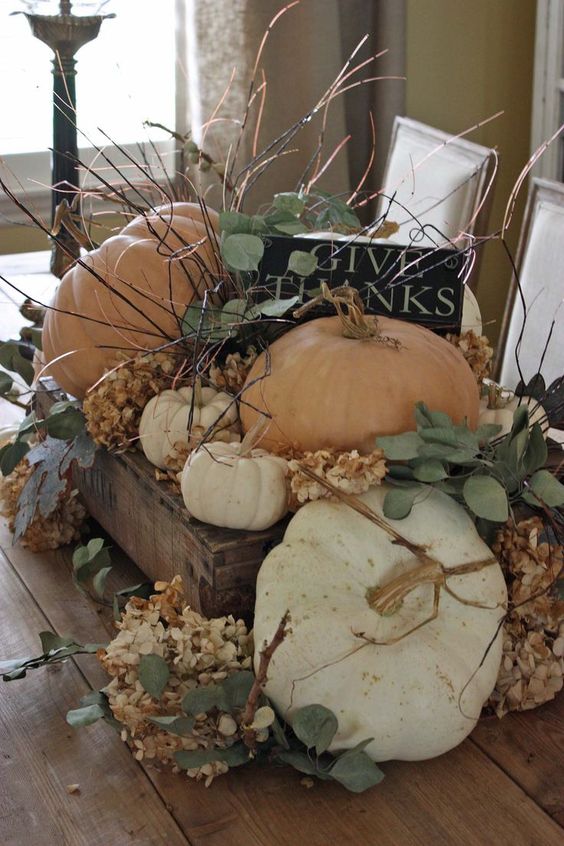 a wooden crate with dried hydrangeas, greenery, pumpkins, a black sign and los of twigs for a rough fall centerpiece