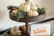 a wooden stand with eucalyptus, white and orange pumpkins and pinecones and a small sign