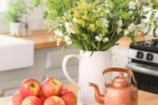 an early fall decoration – a jug with greenery and white blooms, fresh apples and a copper kettle