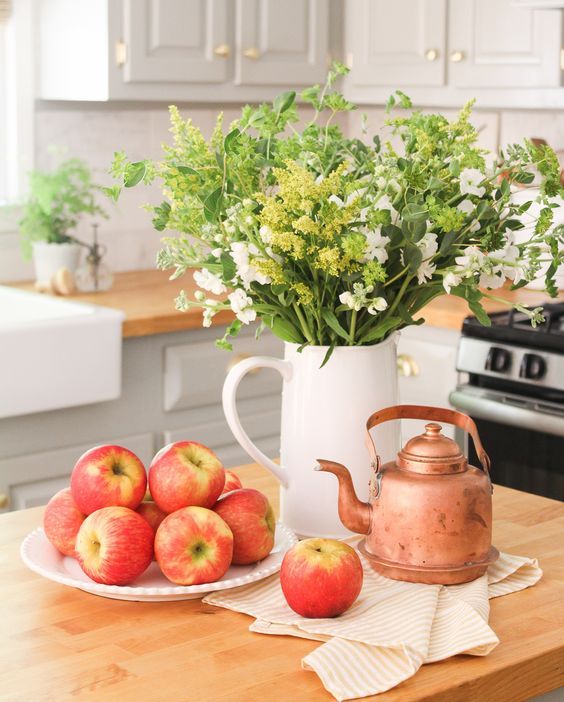 une décoration de début d'automne une cruche avec de la verdure et des fleurs blanches, des pommes fraîches et une bouilloire en cuivre une décoration de début d'automne - une cruche avec de la verdure et des fleurs blanches, des pommes fraîches et une bouilloire en cuivre