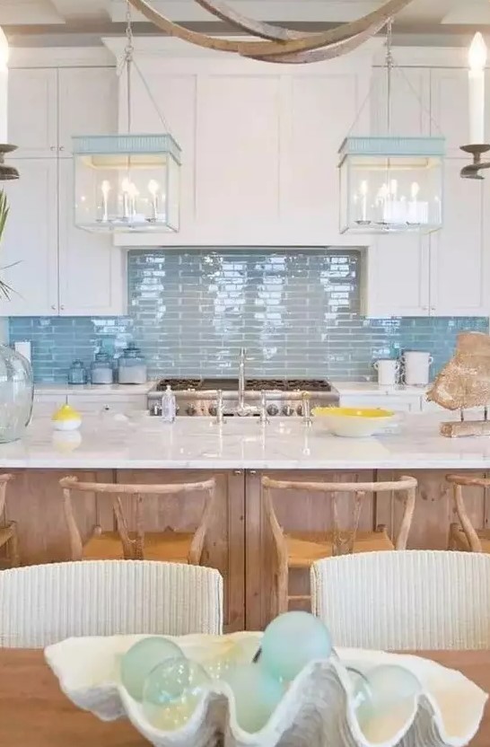 a beach cottage kitchen with white shaker cabinets, a glossy blue tile backsplash, blue and white glass box pendant lamps and a wooden kitchen island