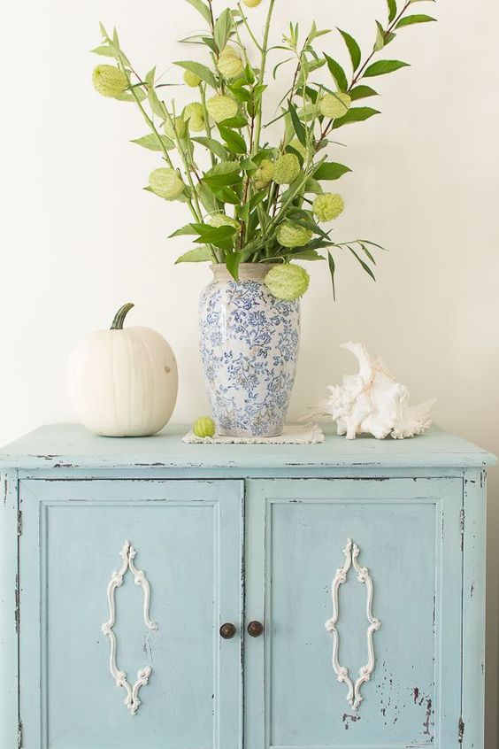 a blue printed vase with blooming branches, a large seashell and a neutral pumpkin for coastal fall decor
