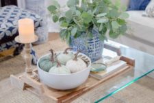 a bowl with neutral fabric pumpkins and a blue pot with greenery plus a candle in a wooden candleholder