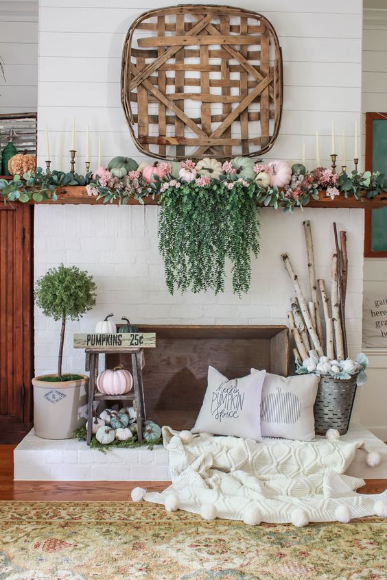 a bright fall mantel with cascadign greenery, pastel pumpkins, greenery, branches in a bucket and a wooden basket